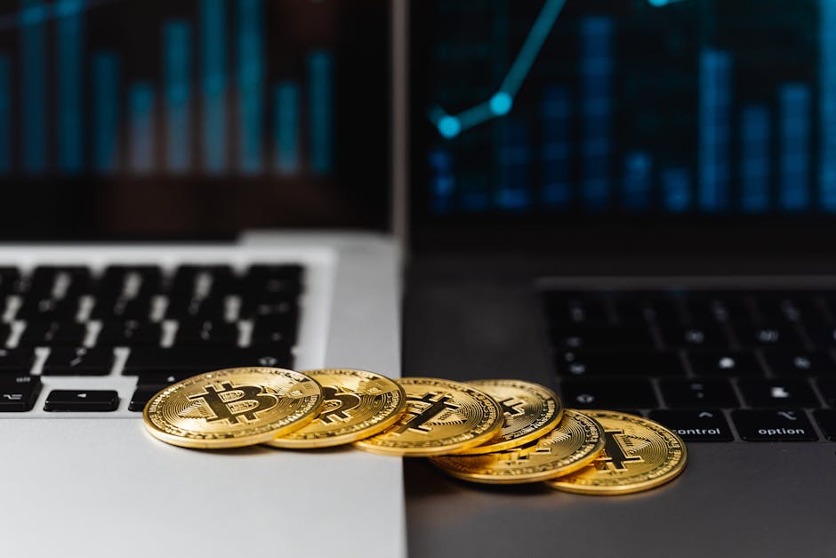 Gold bitcoins placed on laptop keyboards with digital financial graphs in the background